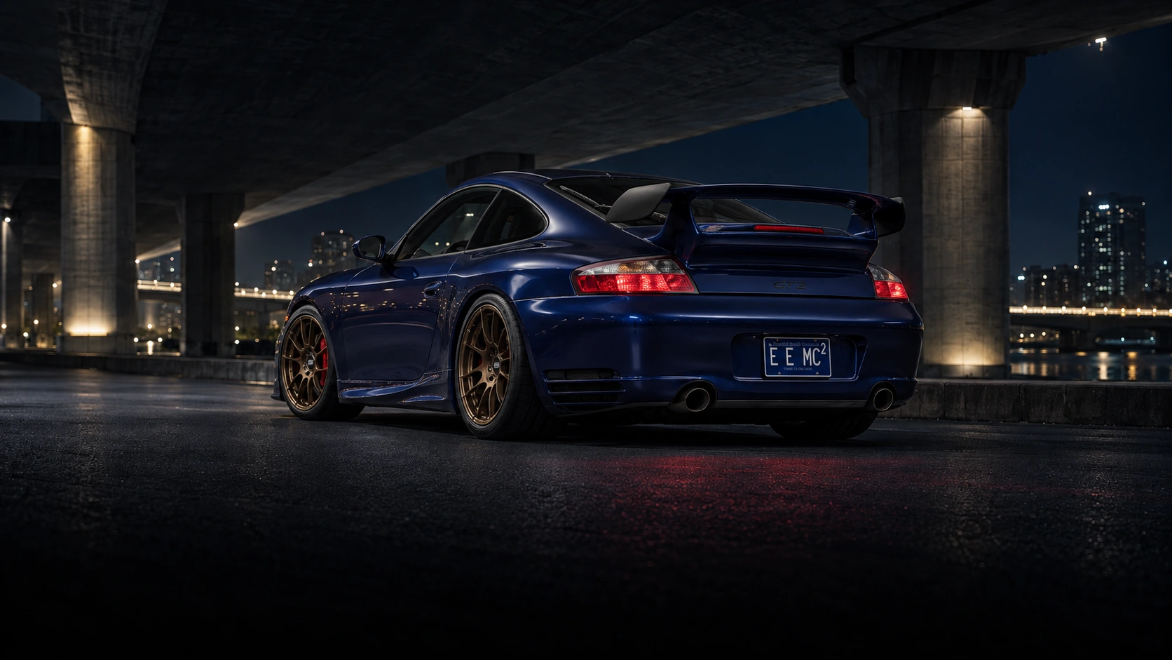 RGB's Lapis Blue Metallic 2001 Porsche 911 Carrera, with bronze BBS wheels and its fixed rear wing, beneath a city overpass after dark.