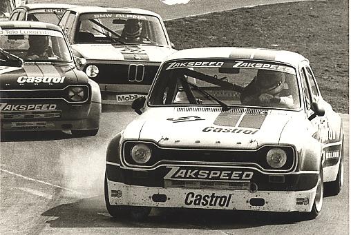 Two black-and-white Group 2 touring cars wheel-to-wheel on track — a Zakspeed-liveried Ford Capri RS in the foreground, a BMW Alpina behind.