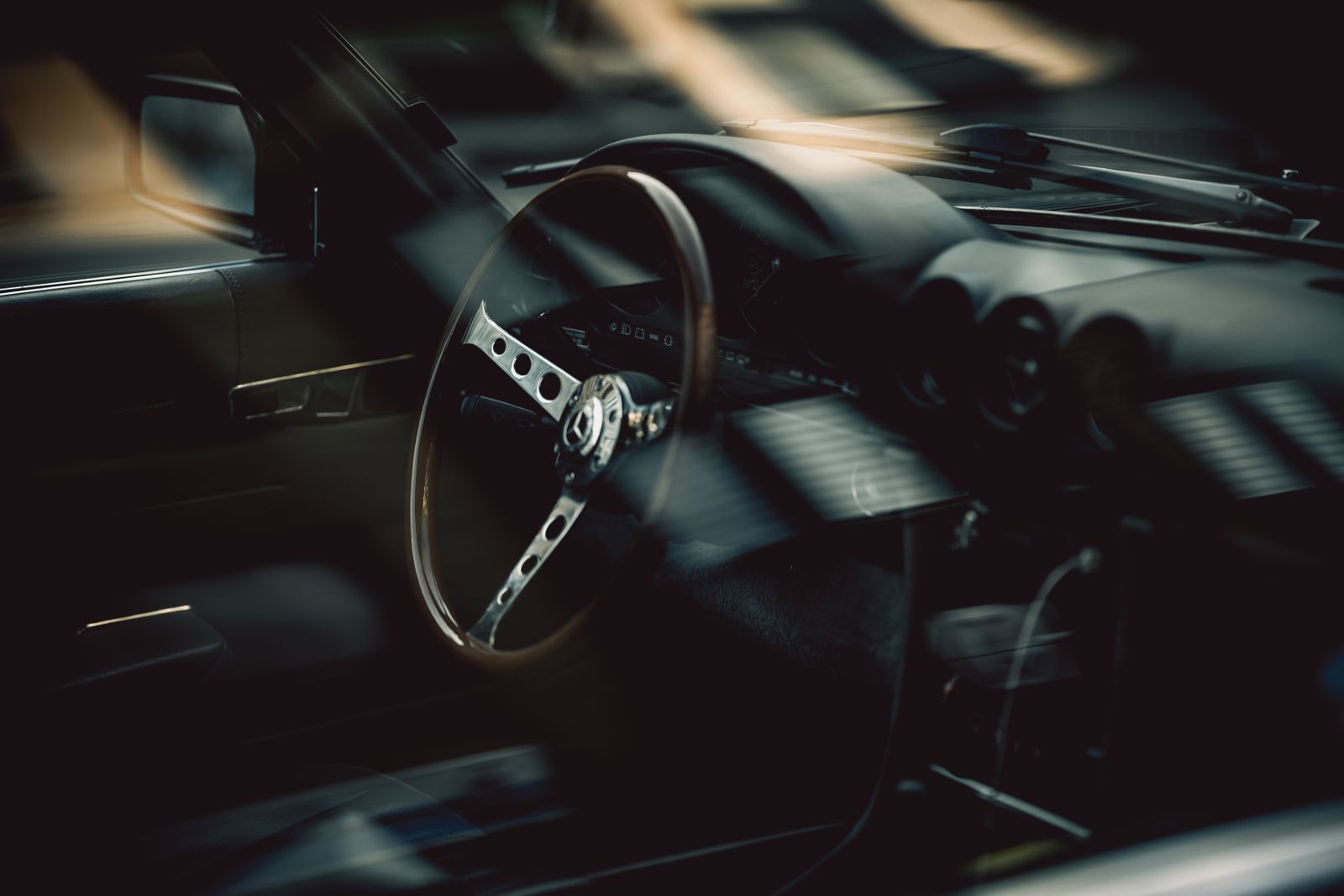 Wood-rimmed steering wheel of a classic car in low light.
