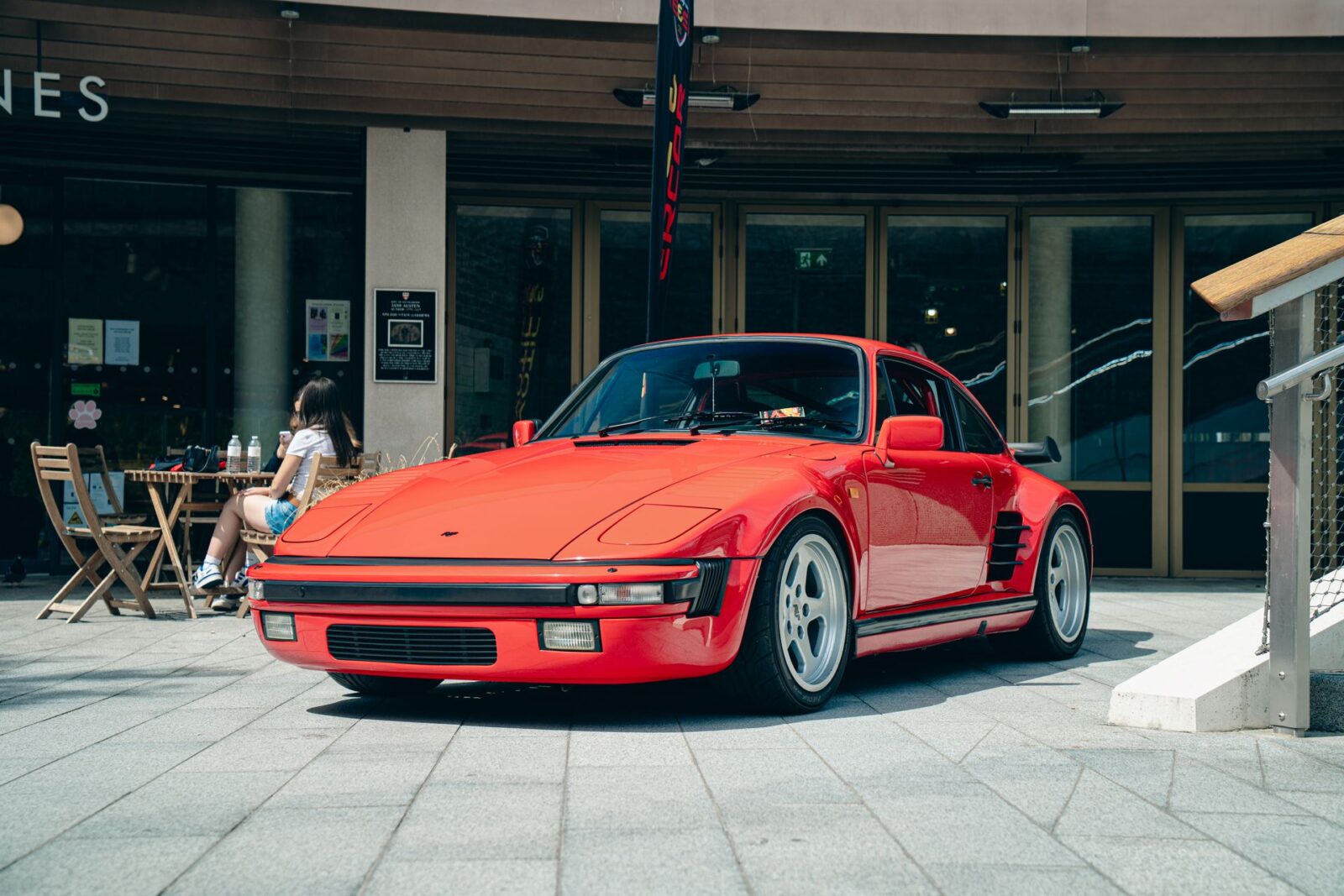 Classic Porsche 930 with slant nose parked before a modern gallery.