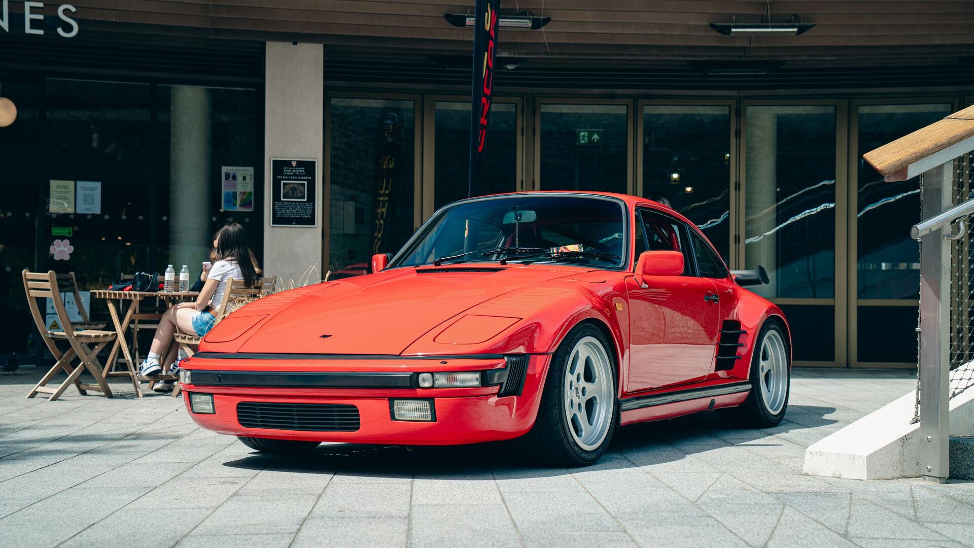Classic Porsche 930 with slant nose parked before a modern gallery.