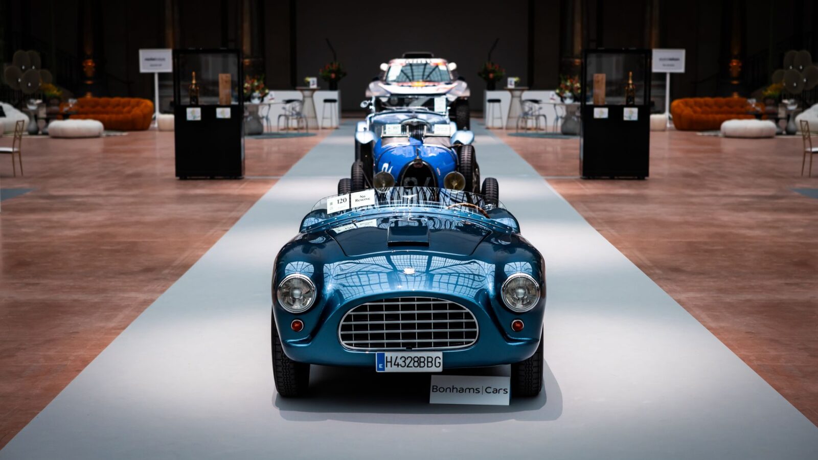 Classic roadster presented on a spotlit platform in a grand hall.