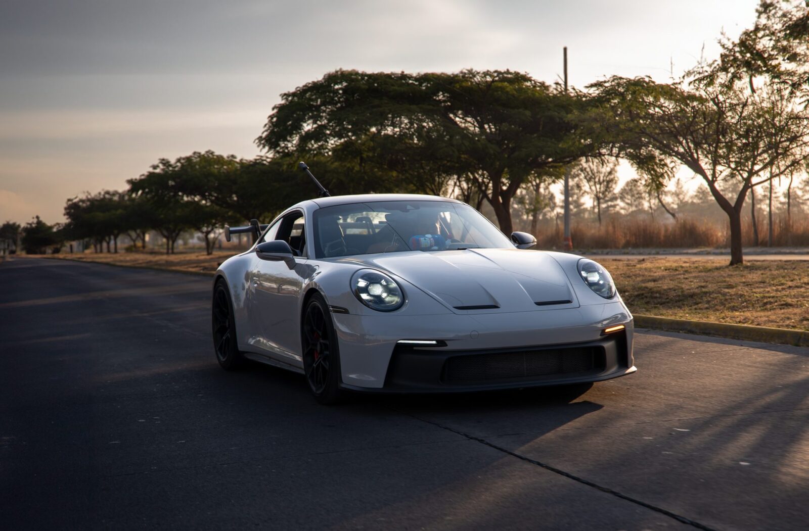 White sports car on a tree-lined road at sunset.